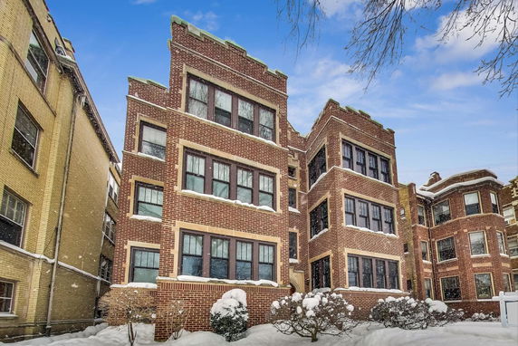 Front view of a multi-story brick apartment building with snow on the ground and windows.