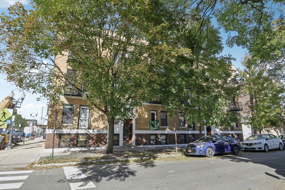 Front view of a multi-story brick building with trees on the sidewalk.