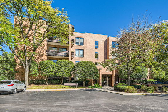 Front view of a multi-story brick apartment building with balconies and surrounding trees.