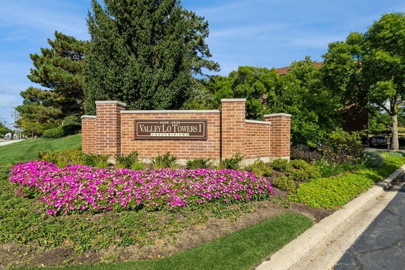 Front view of Valley Lo Towers I condominium sign with brick structure and surrounding landscaping.