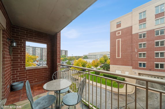 View from a balcony with a table and chairs overlooking surrounding buildings and trees.