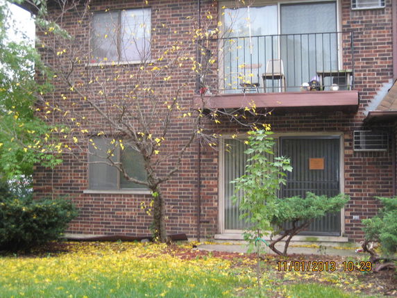 Front view of a brick apartment building with a balcony and ground-level entrance.