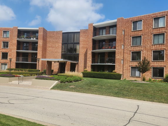 Front view of a multi-story brick apartment building with balconies and large windows.