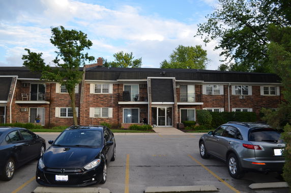 Front view of a two-story brick apartment building with a parking area.