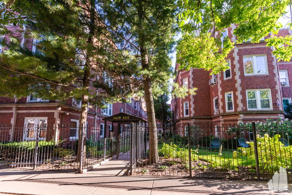 Front view of a multi-story brick apartment building with gated entry.