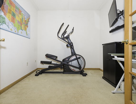 Small room with exercise equipment, a wall-mounted TV, and a map on the wall.