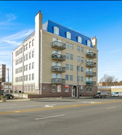 Front view of a multi-story apartment building with balconies and a blue roof.