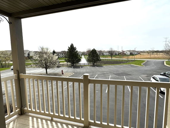 Outdoor view from a balcony overlooking a parking area and distant residential houses.