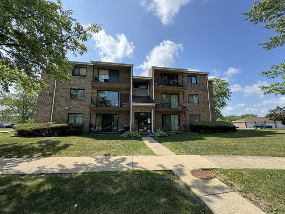 Front view of a three-story brick apartment building with balconies.