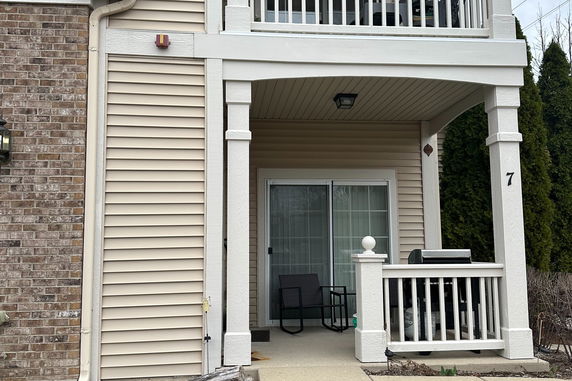 Partial view of the front elevation of a house with a covered porch and sliding glass door.