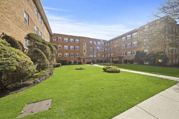 Front view of a multi-story brick apartment building with landscaped green lawn.