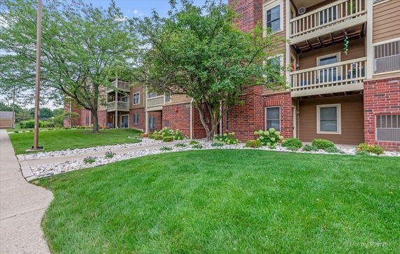 Front view of an apartment building with brick and wood exterior, featuring balconies and landscaped greenery.