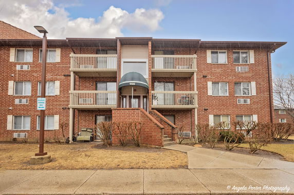 Front view of a three-story brick apartment building with balconies.