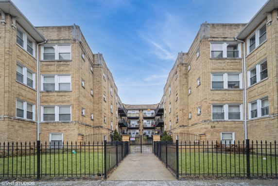 Front view of a multi-story brick apartment building with a gated entrance.
