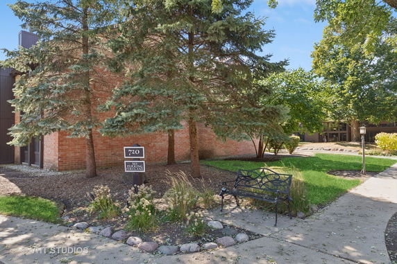 Front view of a brick building with trees and a bench.