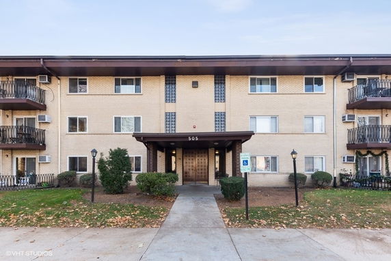 Front view of a three-story apartment building with balconies and entrance canopy.