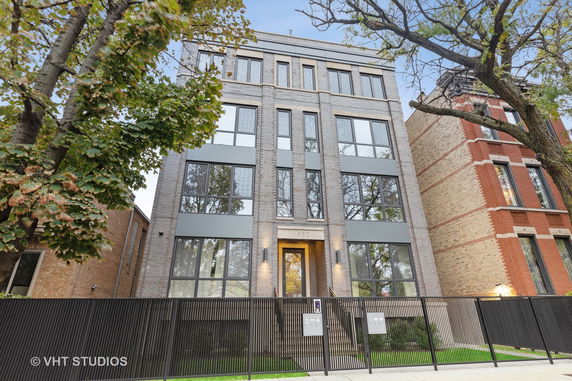 Front view of a multi-story modern building with large windows and a fenced entrance.