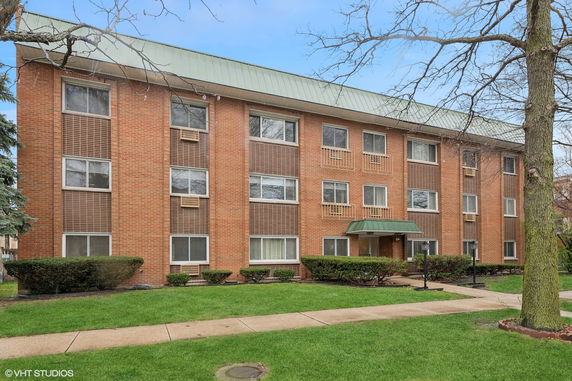 Front view of a three-story brick apartment building with multiple windows and a green roof.