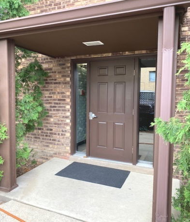 Front view of a building entrance with a brown door and brick exterior.