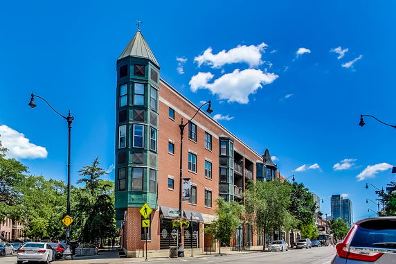 Front view of a multi-story, brick building with a corner tower and street-level shops.