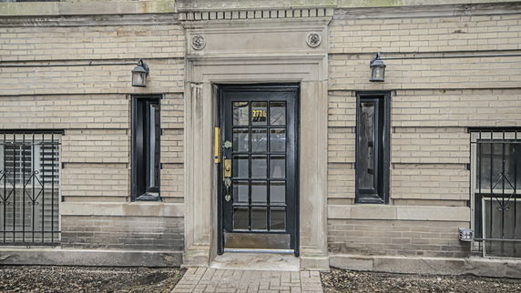 Front view of a brick building entrance with a black door and two lamps.
