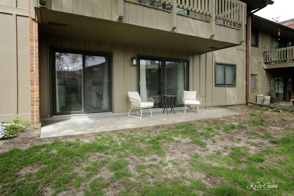 Front view of a house with sliding glass doors leading to a patio and two chairs.