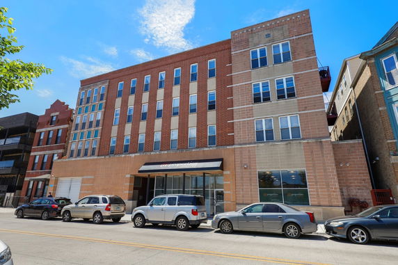 Front view of a multi-story brick building with parked cars in front.