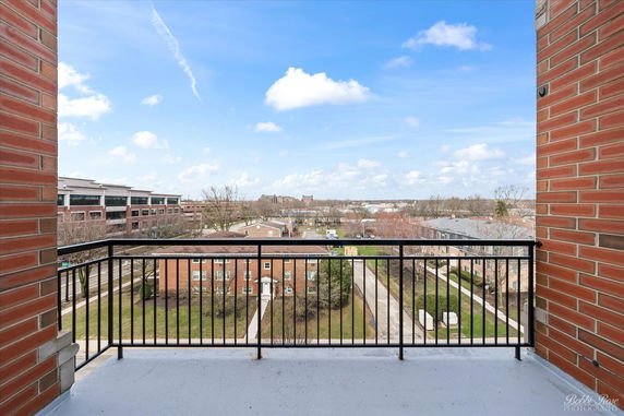 View from a balcony showing a cityscape with buildings and trees in the distance.