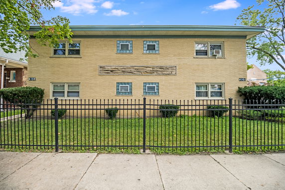 Front view of a two-story brick building with multiple windows and a surrounding fence.