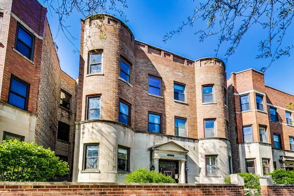 Front view of a multi-story brick building with cylindrical and rectangular extensions.