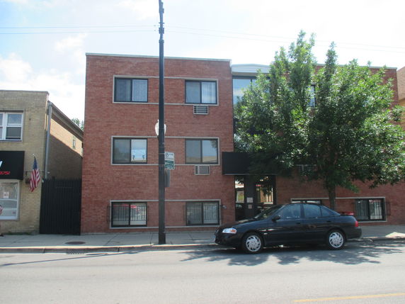 Front view of a three-story brick building with a tree and parked car.