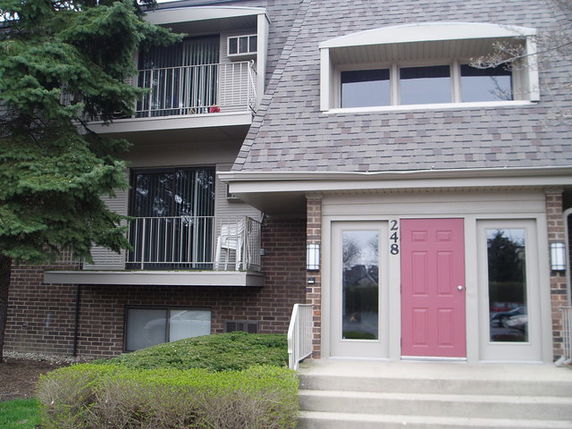 Front view of a multi-story brick building with balconies and a red door entrance.