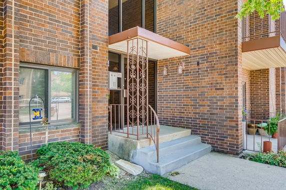 Front entrance of a brick building with steps leading to a door and decorative metal railing.