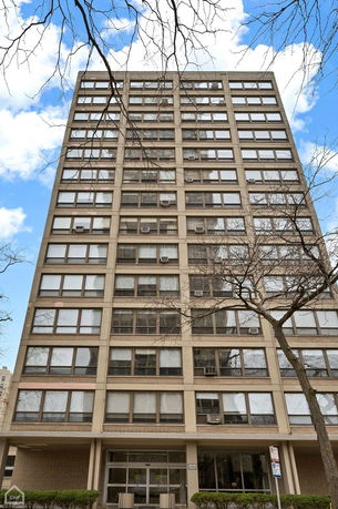 Front view of a multi-story building with large windows and air conditioning units on a cloudy day.