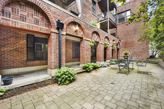 Front view of a brick residential building with arched doorways and a small patio area.