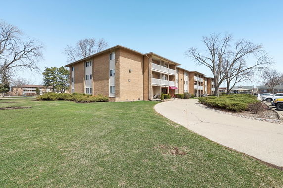 Front view of a three-story apartment building with a pathway and greenery.