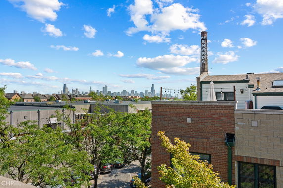 Panoramic view of city skyline with buildings and tree-lined street in the foreground.