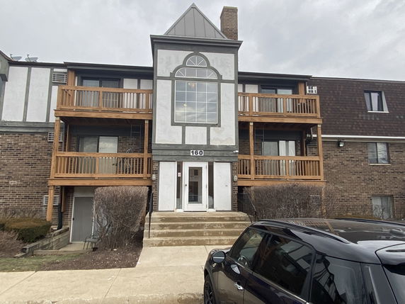 Front view of a multi-story building with wooden balconies and brick exterior.