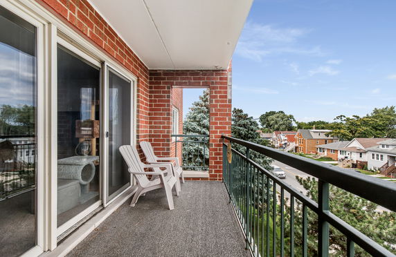 Balcony with brick walls and railing overlooking residential neighborhood.