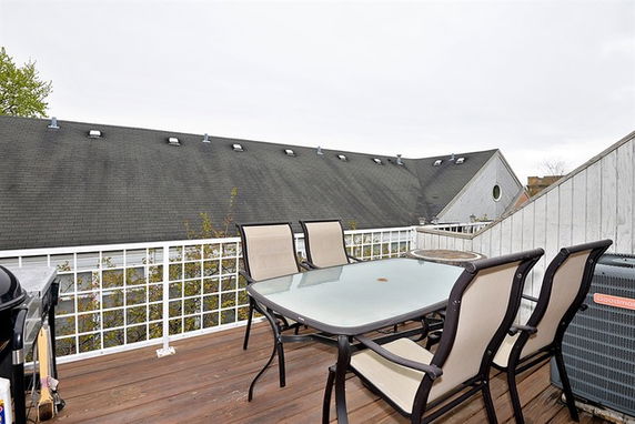 Rooftop patio with table and chairs, surrounded by railings, adjacent to neighboring roofs.