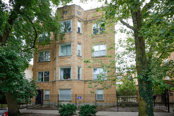Front view of a multi-story brick apartment building with several windows and a gated entrance.