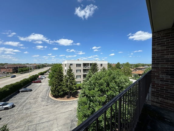 Panoramic view from a balcony overlooking a parking area and adjacent buildings.