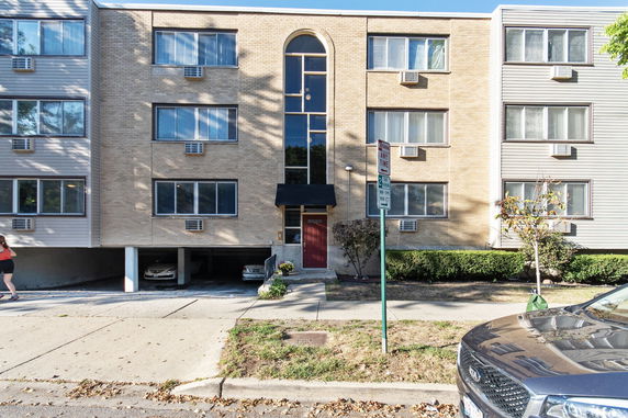 Front view of a multi-story apartment building with a brick facade and parking area underneath.