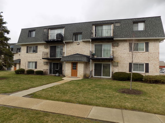 Front view of a three-story residential building with balconies and a central entrance.