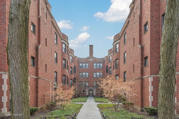 Front view of a multi-story brick apartment building with a central walkway and garden area.