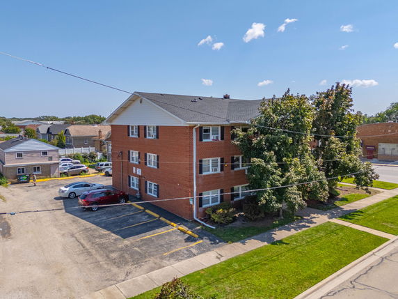 Front view of a three-story brick apartment building with parking spaces.