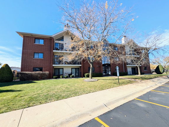 Front view of a multi-story brick apartment building with balconies and a landscaped lawn.