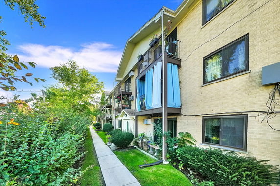 Front view of a three-story apartment building with balconies and greenery.