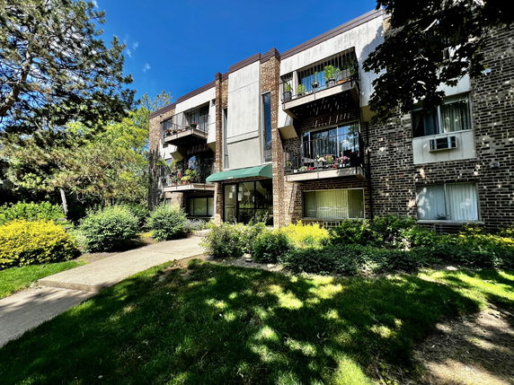 Front view of a multi-story apartment building with balconies and a green entrance canopy.