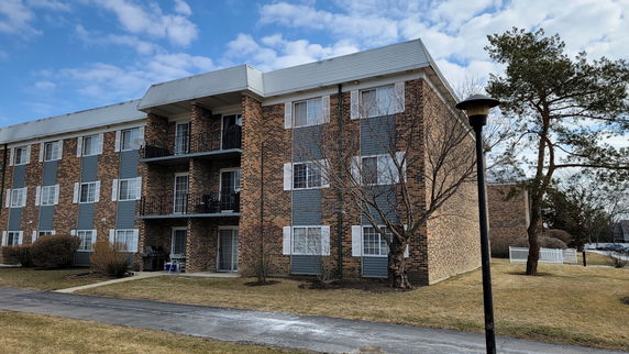Front view of a three-story brick apartment building with balconies.